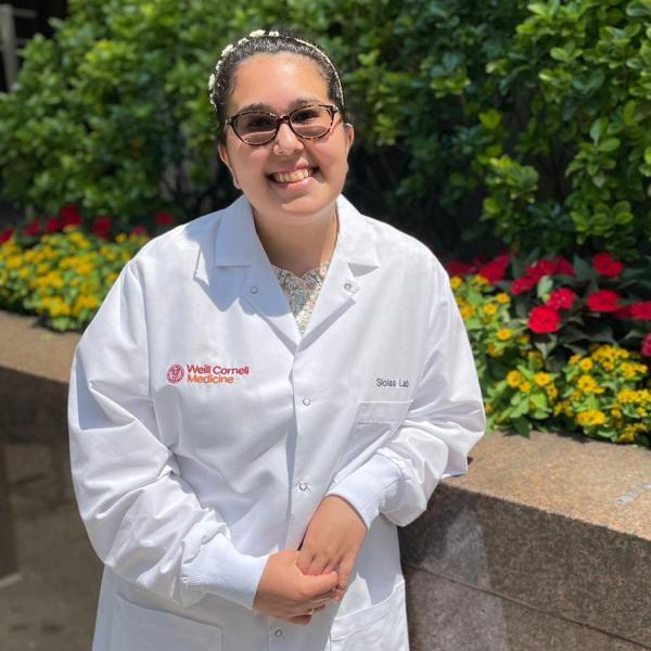 Alison Juray standing in front of flowers in a lab coat